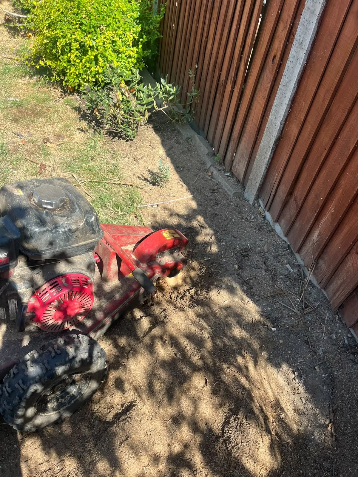 Stump grinding equipment beside disturbed soil along a timber garden fence
